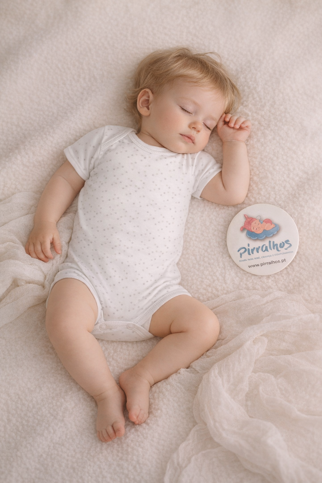 Bebé dormindo de body branco com padrão de estrelas e placa com logo Pirralhos