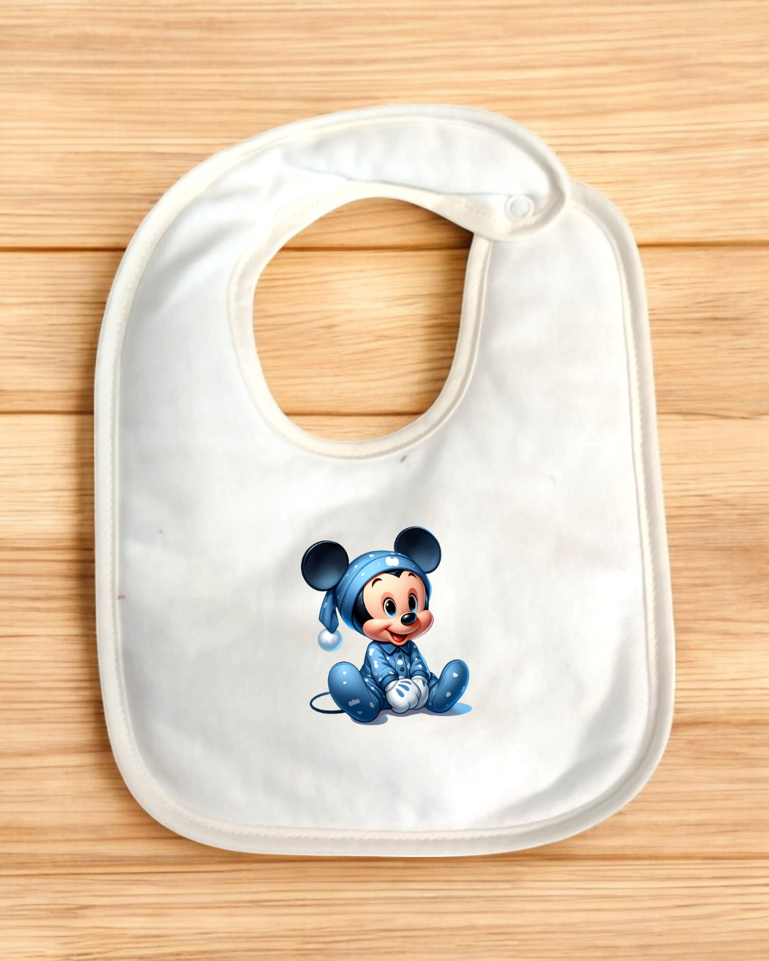 Babete branco com estampa de rato bebê azul sobre superfície de madeira clara