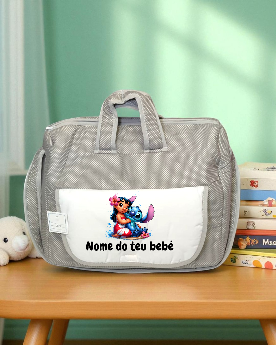 Mala de bebé cinzenta com bolso branco, ilustração e texto, numa mesa de madeira com brinquedo e livros