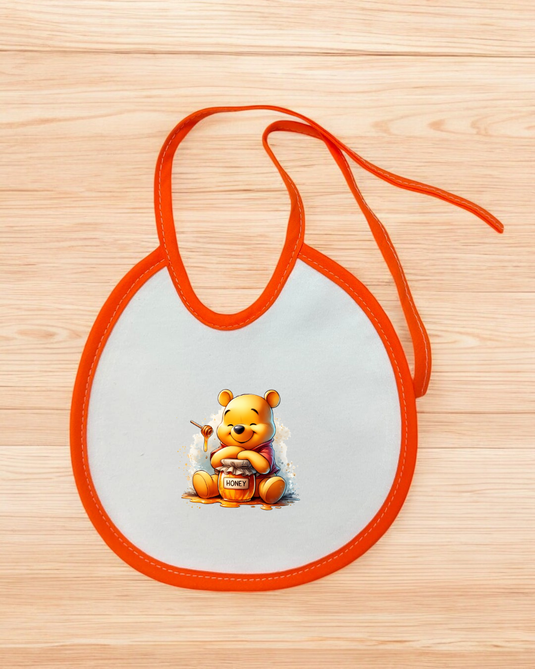 Babete branco com bordas laranja e imagem do Winnie the Pooh com pote de mel