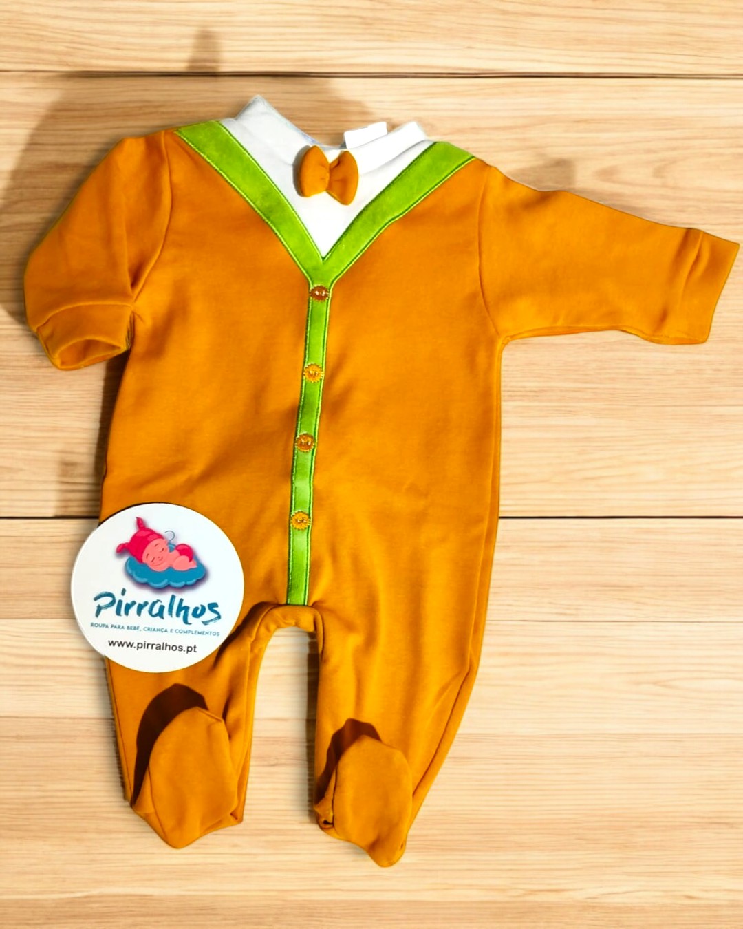 Macacão de bebé laranja com detalhes verdes e branca, etiqueta da marca Pirralhos, sobre fundo de madeira