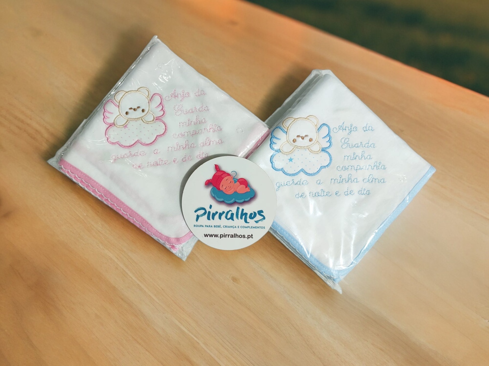 Dois panos de bebé bordados em algodão rosa e azul em mesa de madeira clara.