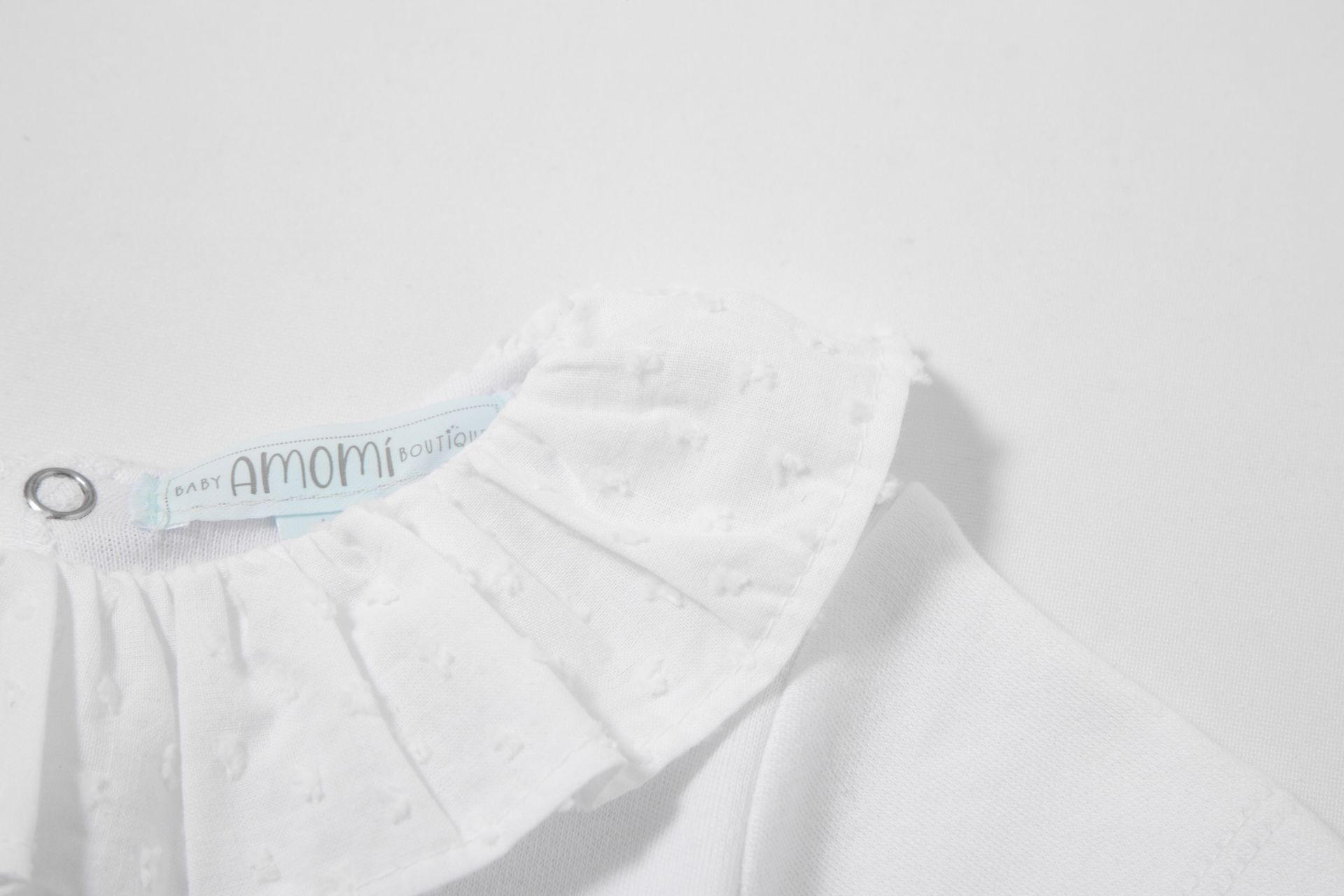 Blusa branca de bebé com gola rodada franzida e etiqueta AMOMI