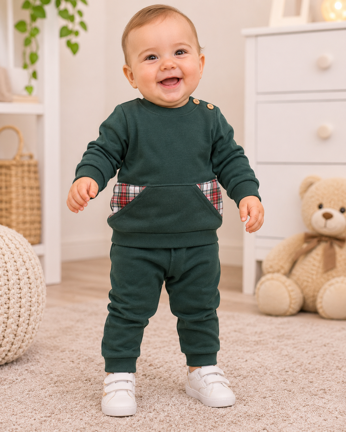 Bebé sorridente vestido com conjunto verde escuro com bolsos xadrez e sapatilhas brancas