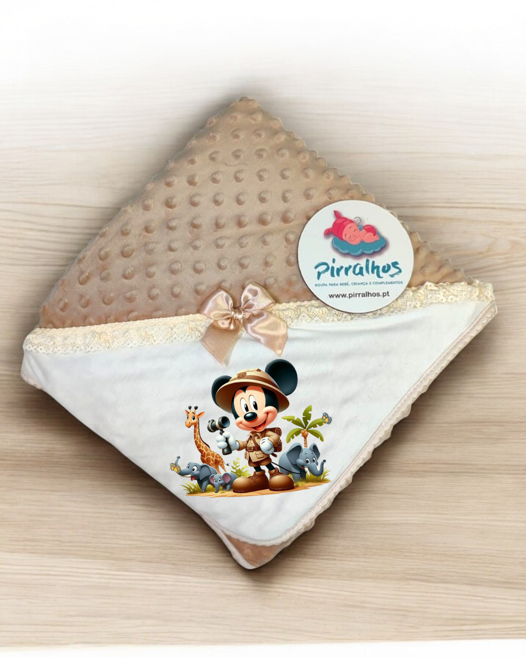 Manta castanha com textura, tecido branco com renda, laço bege, estampa do Mickey Mouse e etiqueta Pirralhos