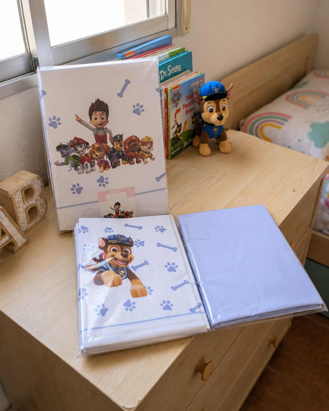 Conjunto de roupa de cama Patrulha Pata embalado sobre cómoda de madeira com livros e peluche ao lado