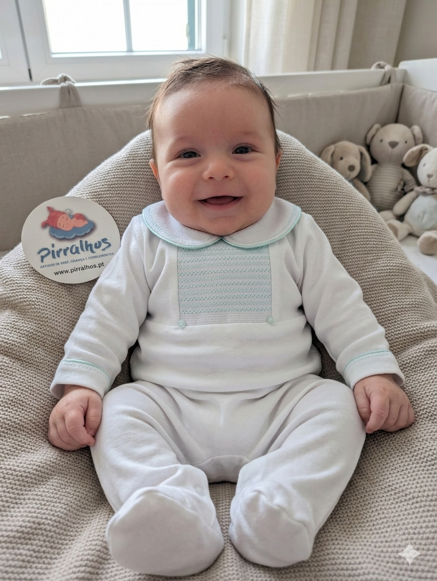 Bebé vestido com macacão branco de gola arredondada com detalhes azuis sentado em almofada bege com peluches ao fundo