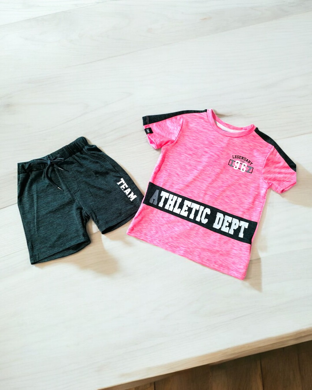 Conjunto de roupa desportiva rosa e preta com calções pretos sobre superfície de madeira clara