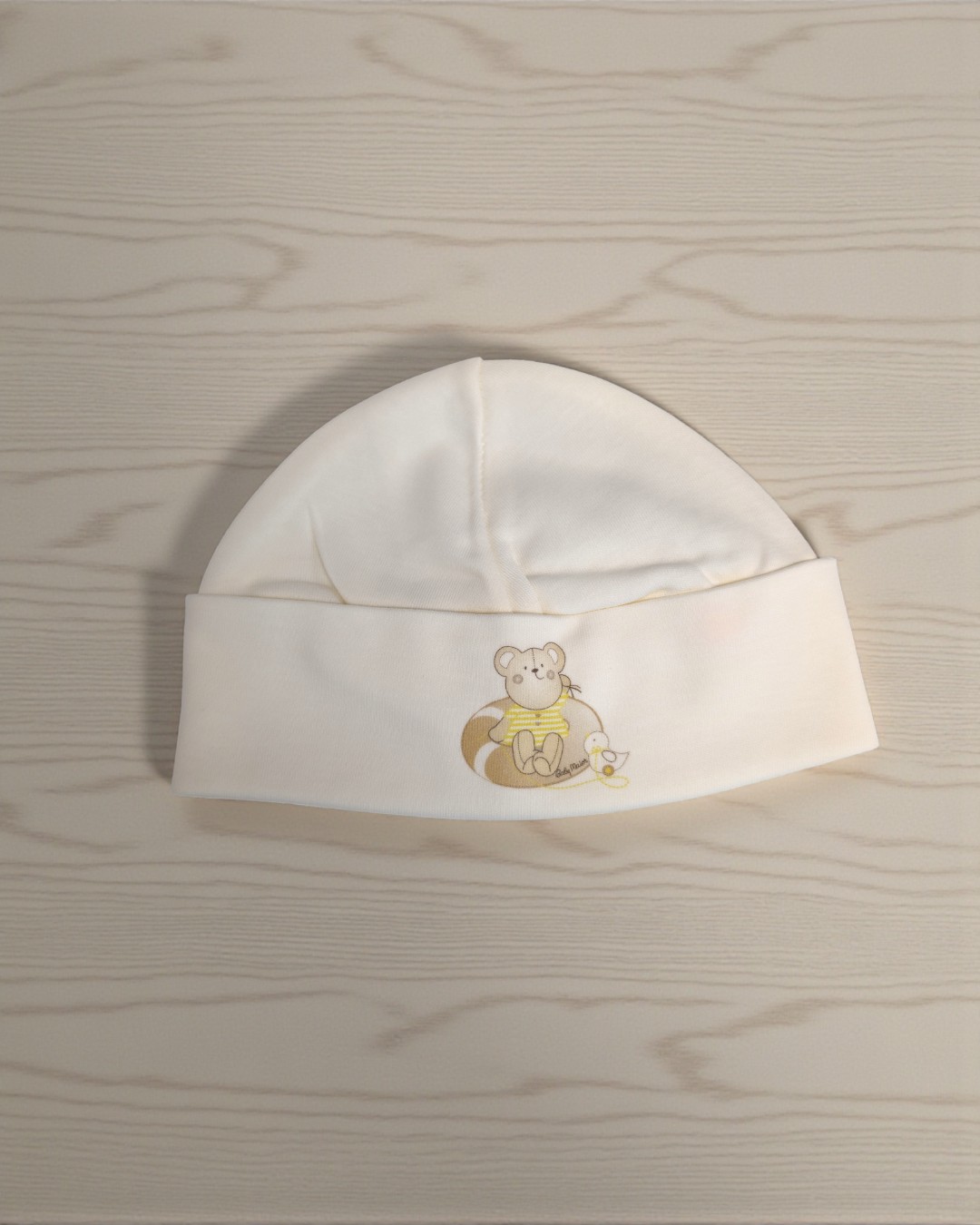Gorro de bebé branco com estampa de ursinho e pato, sobre madeira clara