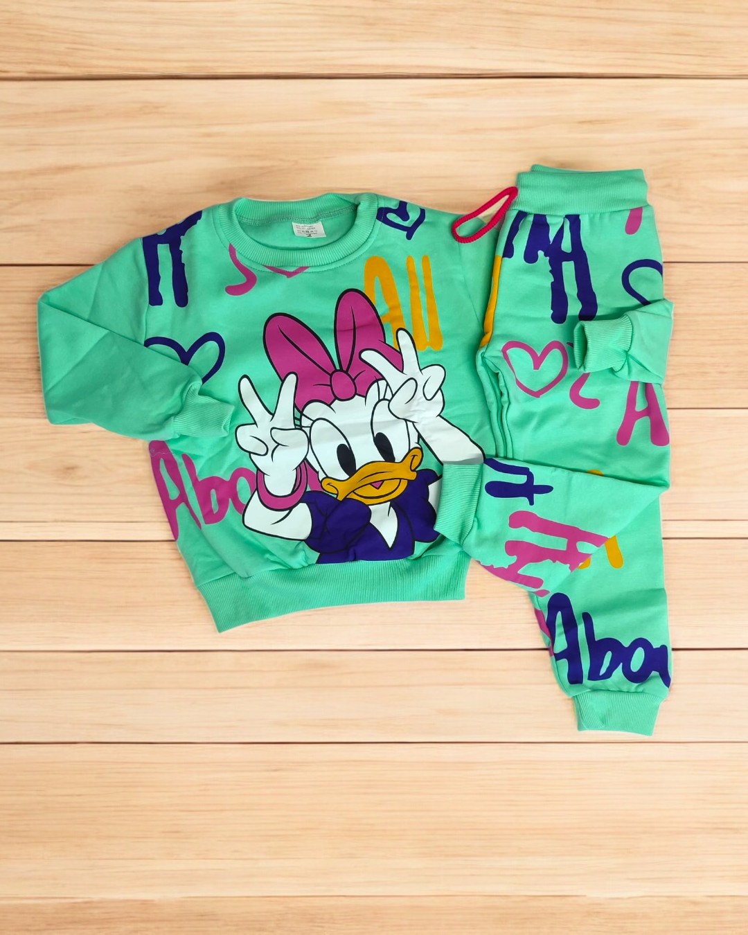 Conjunto de roupa infantil verde com estampa da personagem Daisy Duck e padrões multicoloridos