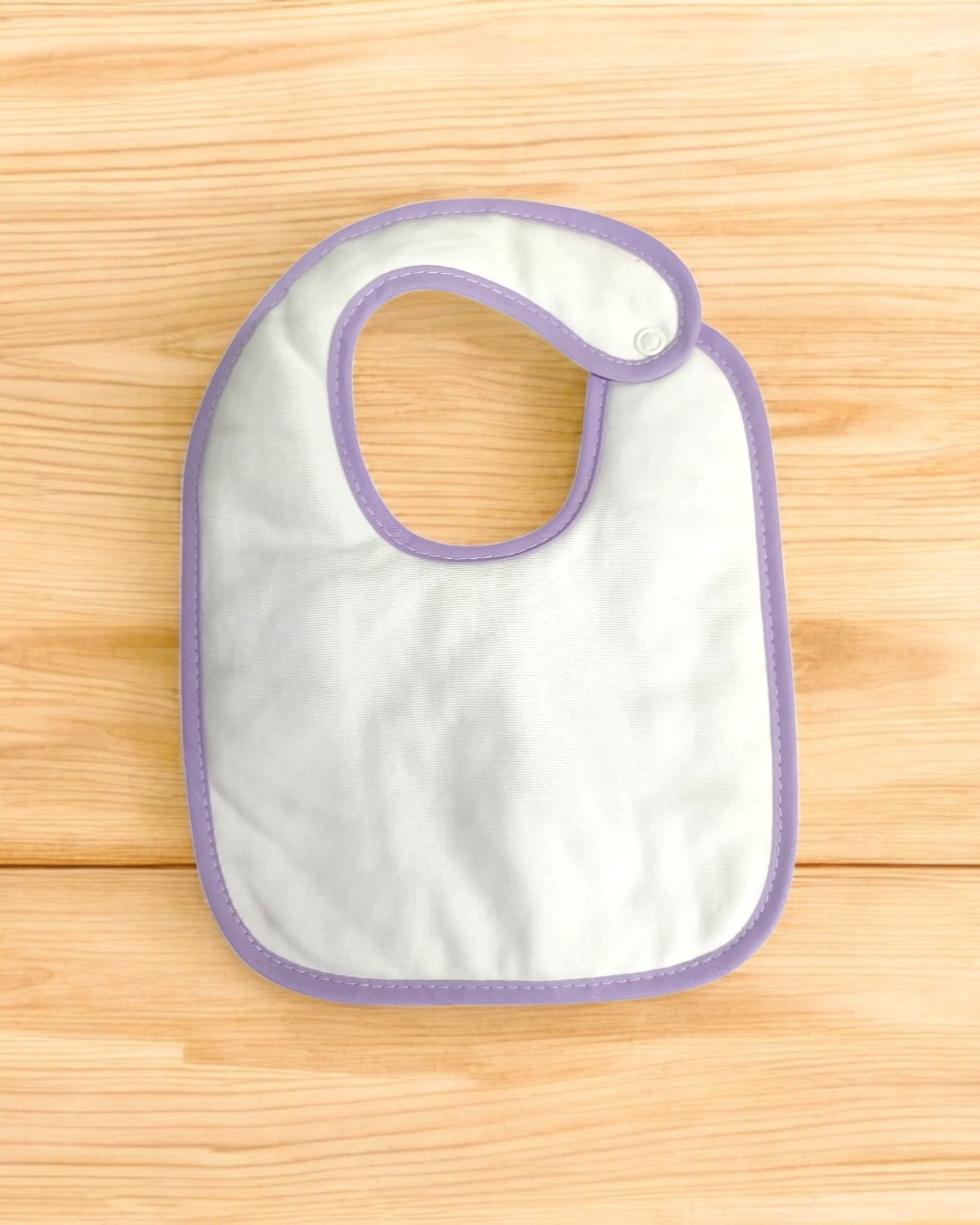 Babete branco com bordas lilás sobre superfície de madeira clara
