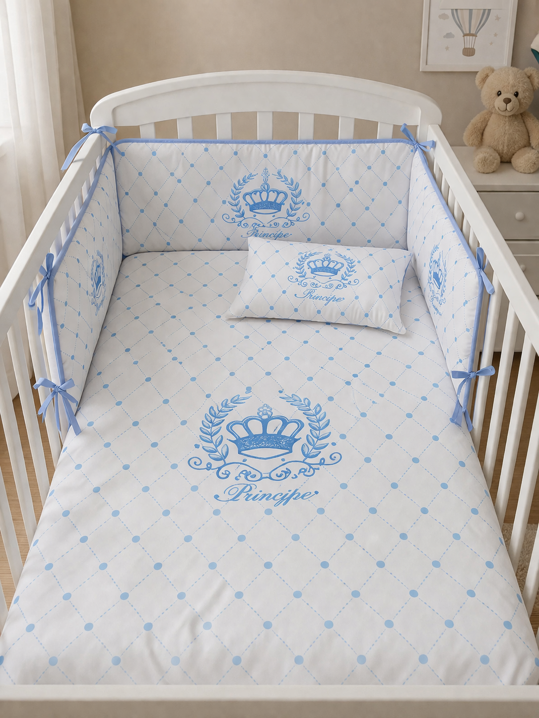 Berço branco com roupa de cama branca e azul decorada com coroas e padrão xadrez