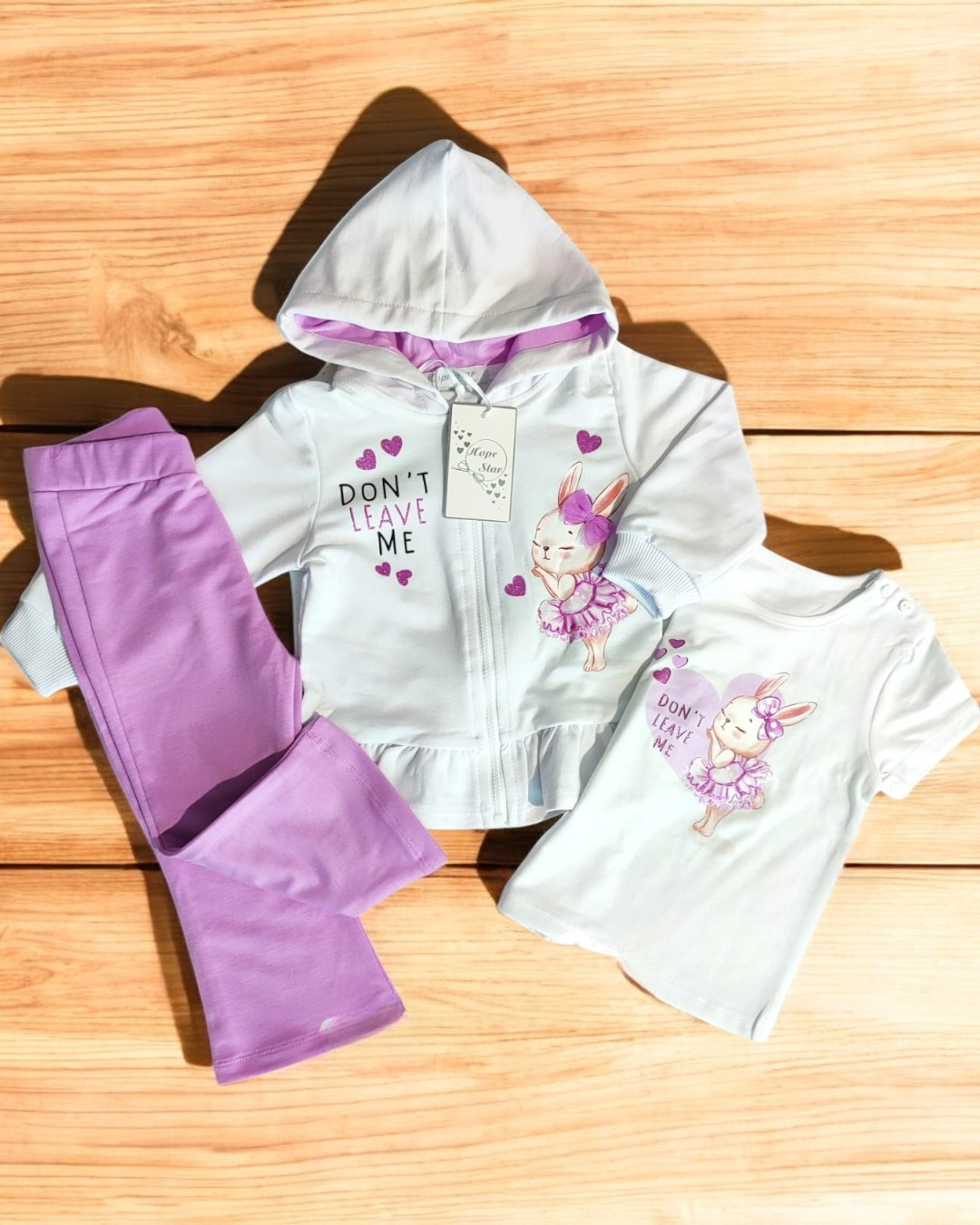 Conjunto infantil branco e lilás com estampa de coelha e texto, calças lilás, casaco com capuz e t-shirt.