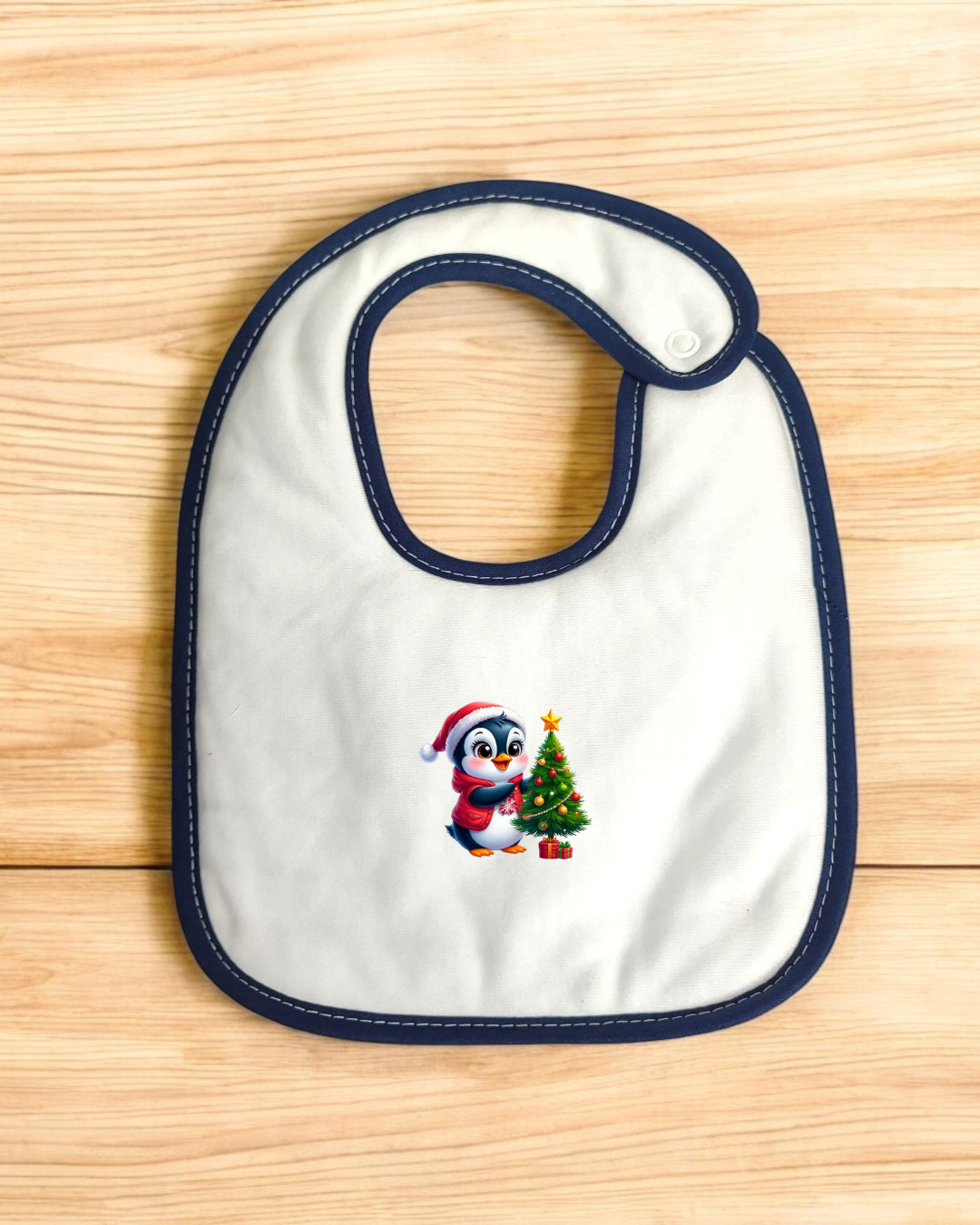 Babete branco com bordas azuis e pinguim decorativo a enfeitar árvore de Natal.