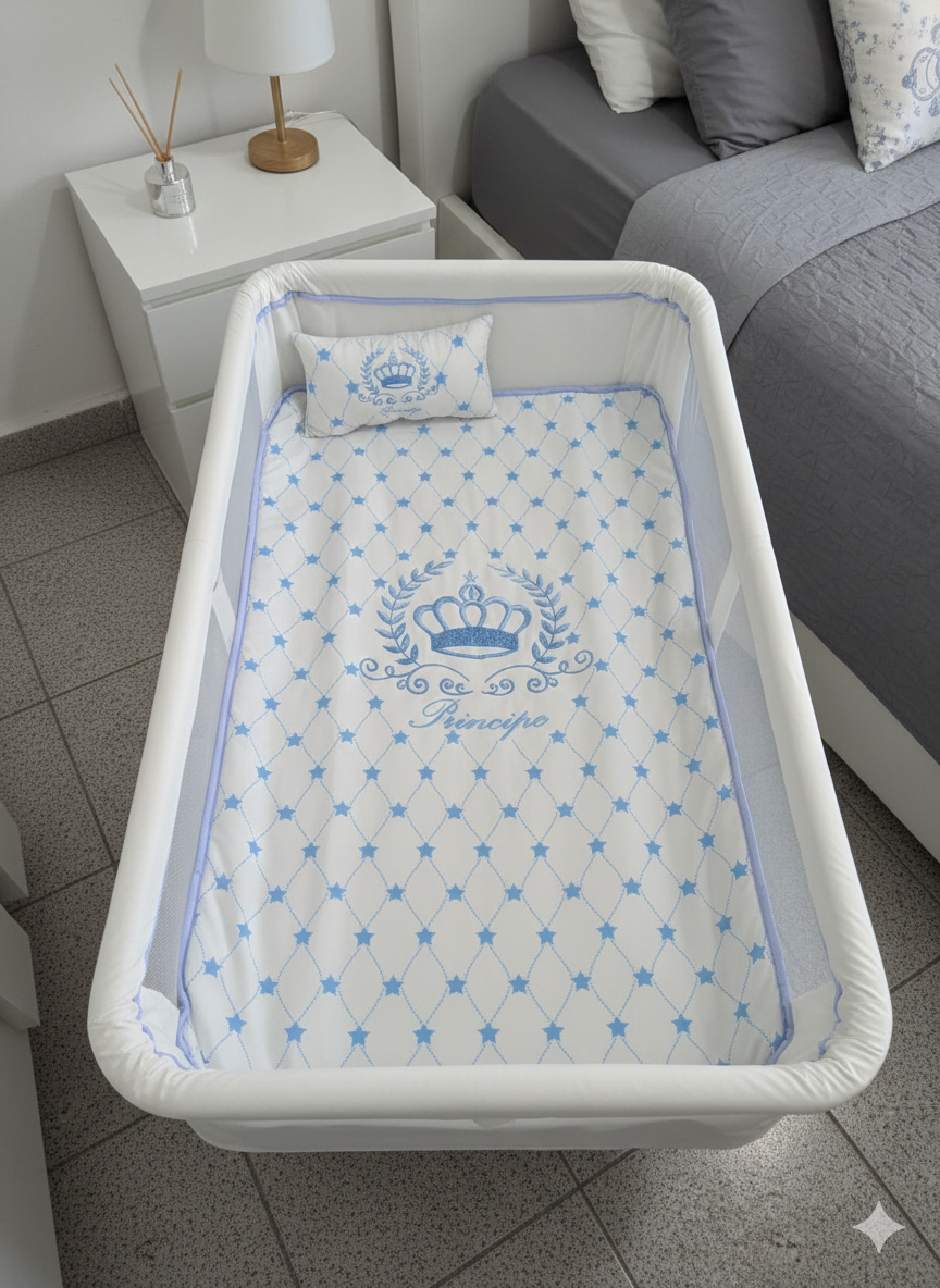 Berço branco com colchão e almofada decorados em azul, ao lado de mesa de cabeceira branca com difusor e candeeiro