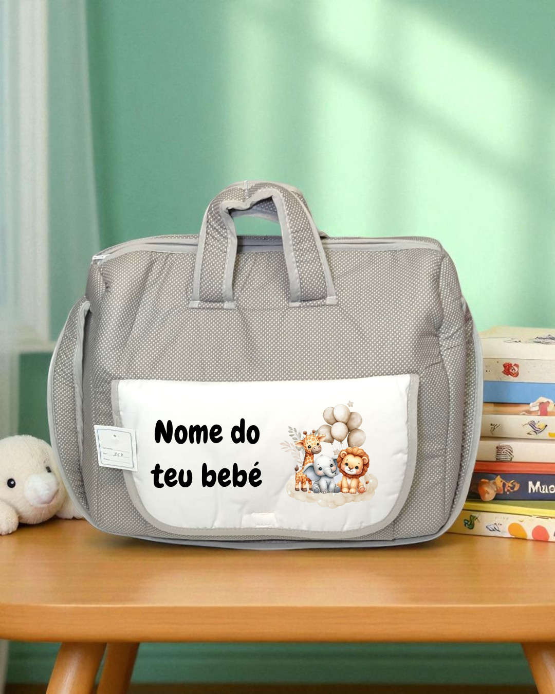 Mala cinzenta de tecido com bolso branco estampado com animais e texto, em mesa de madeira com peluche e livros.