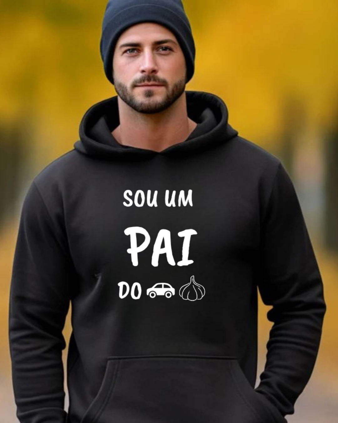 Homem com sweatshirt preta com texto 'SOU UM PAI DO' e emojis de carro e alho, gorro preto e fundo amarelo desfocado.