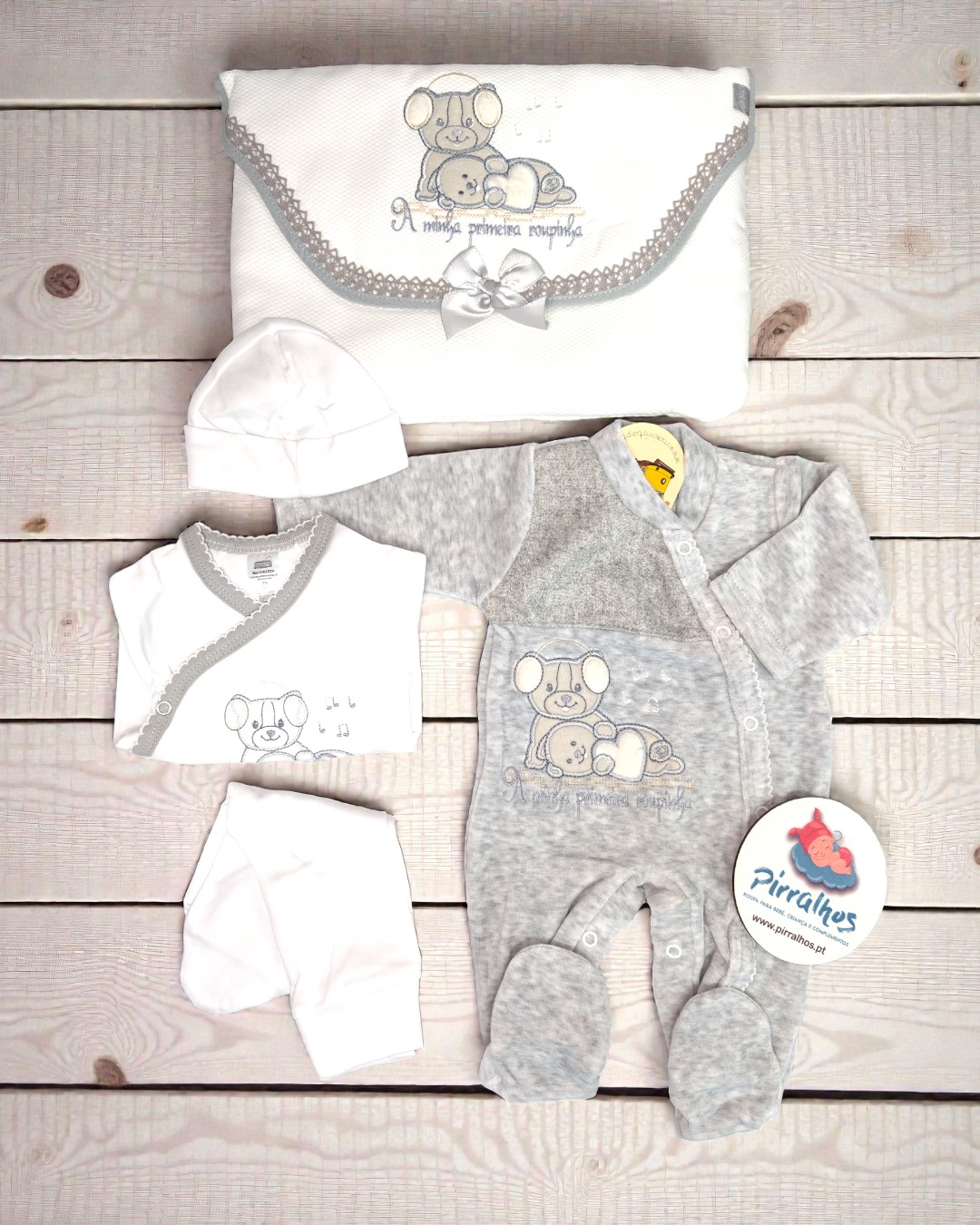 Conjunto de roupa para bebé branca e cinzenta com ursinho bordado e texto sobre madeira clara
