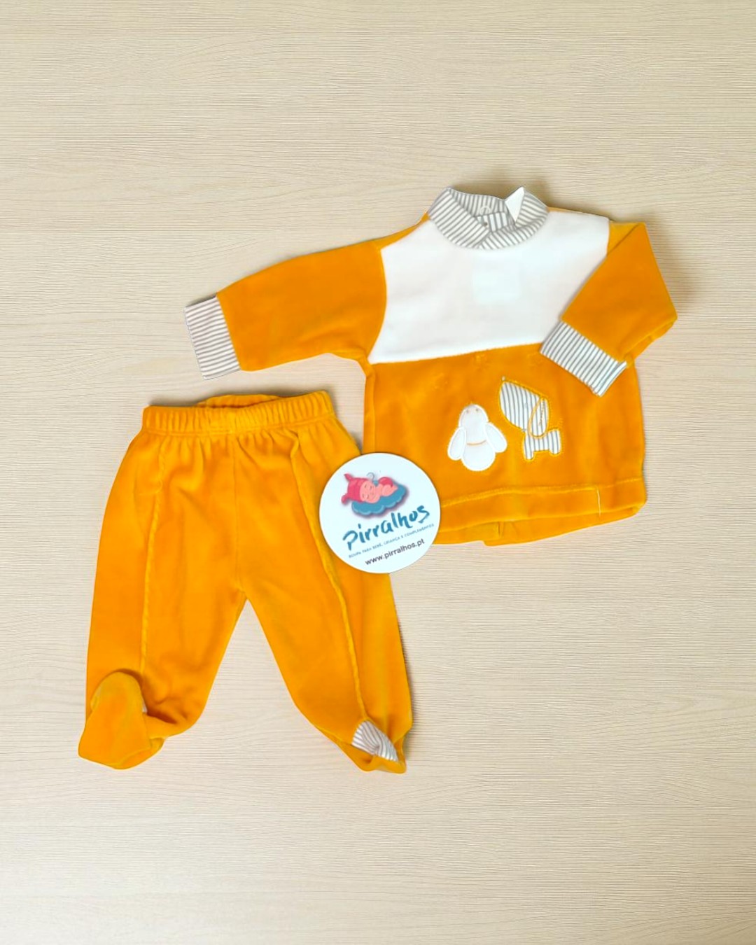 Conjunto de bebé em tecido laranja e branco com padrão de coelhos e gola às riscas.