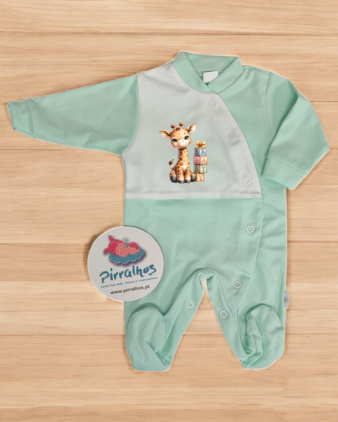Macacão de bebé verde e branco com desenho de girafa e texto BABY sobre fundo de madeira