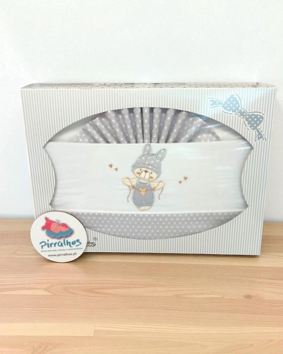 Caixa branca com roupa de bebé cinzenta com padrão de bolinhas e coelho bordado