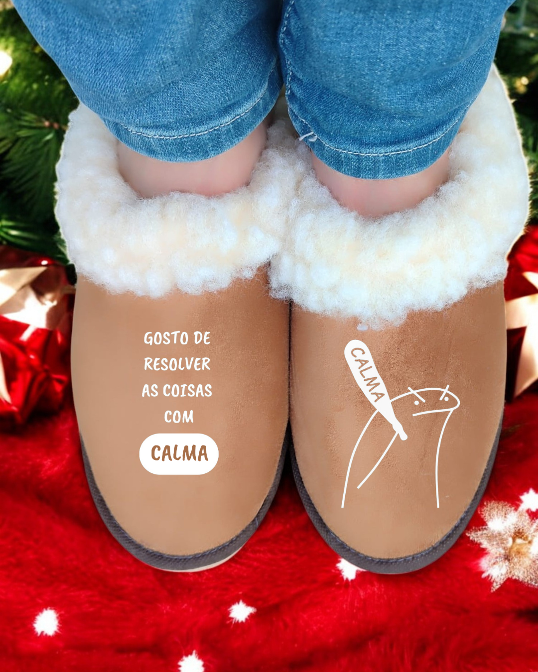 Chinelos castanhos forrados com pelúcia branca e texto impresso, usados por uma pessoa com calças de ganga, sobre superfície vermelha com decoração.