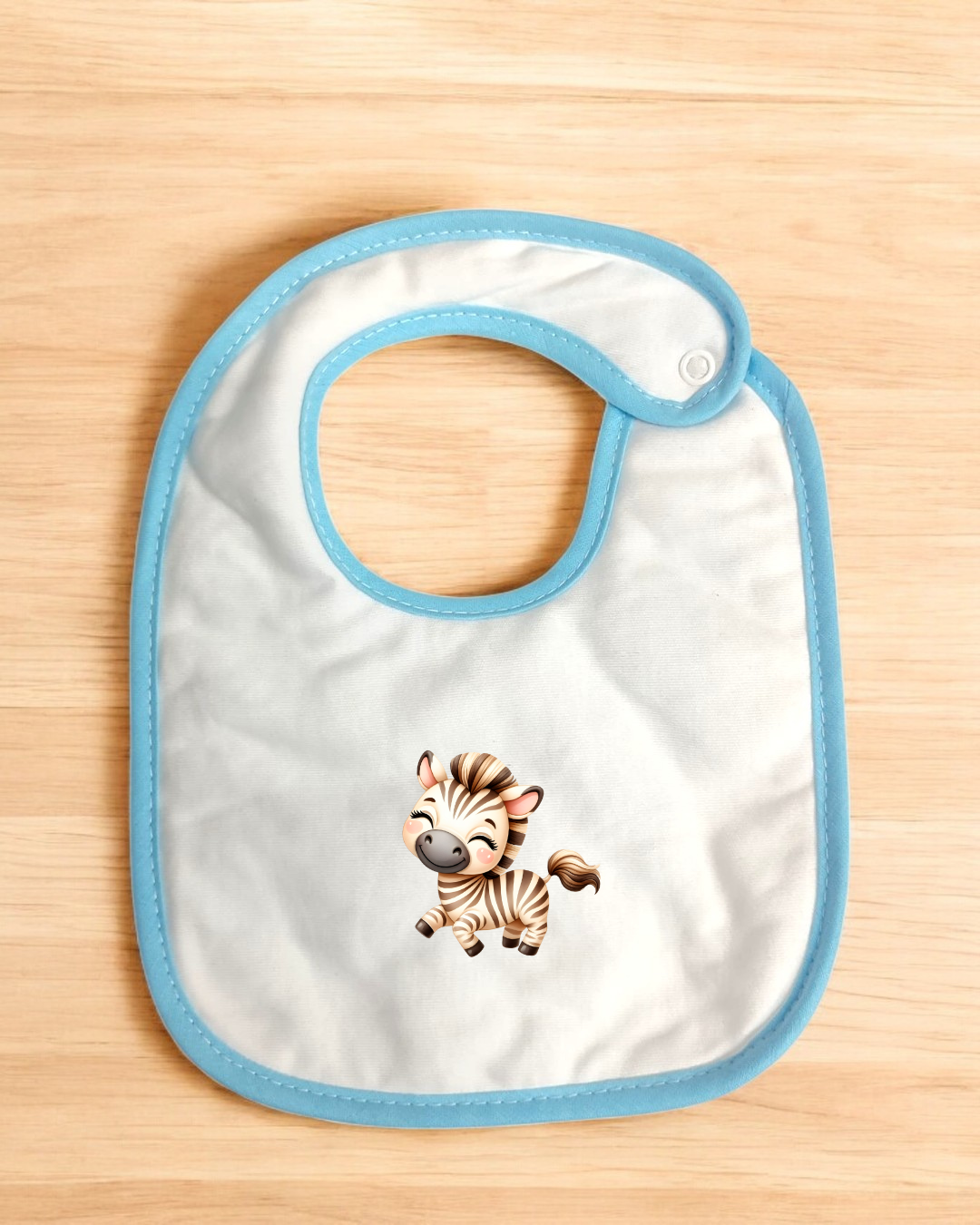 Babete branco com borda azul e desenho de zebra sobre superfície de madeira clara