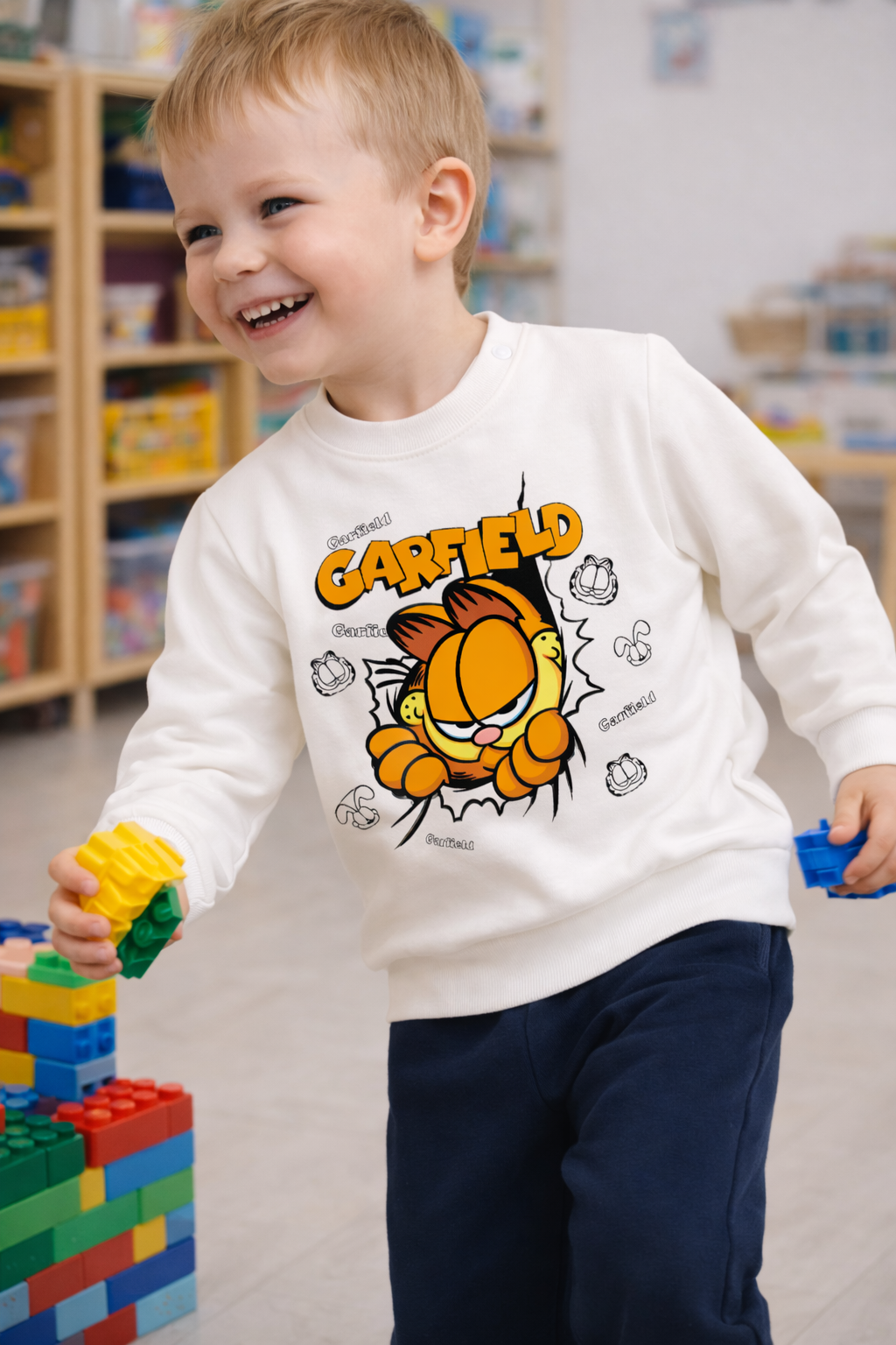 Camisola branca de criança com Garfield em ambiente interior com brinquedos.