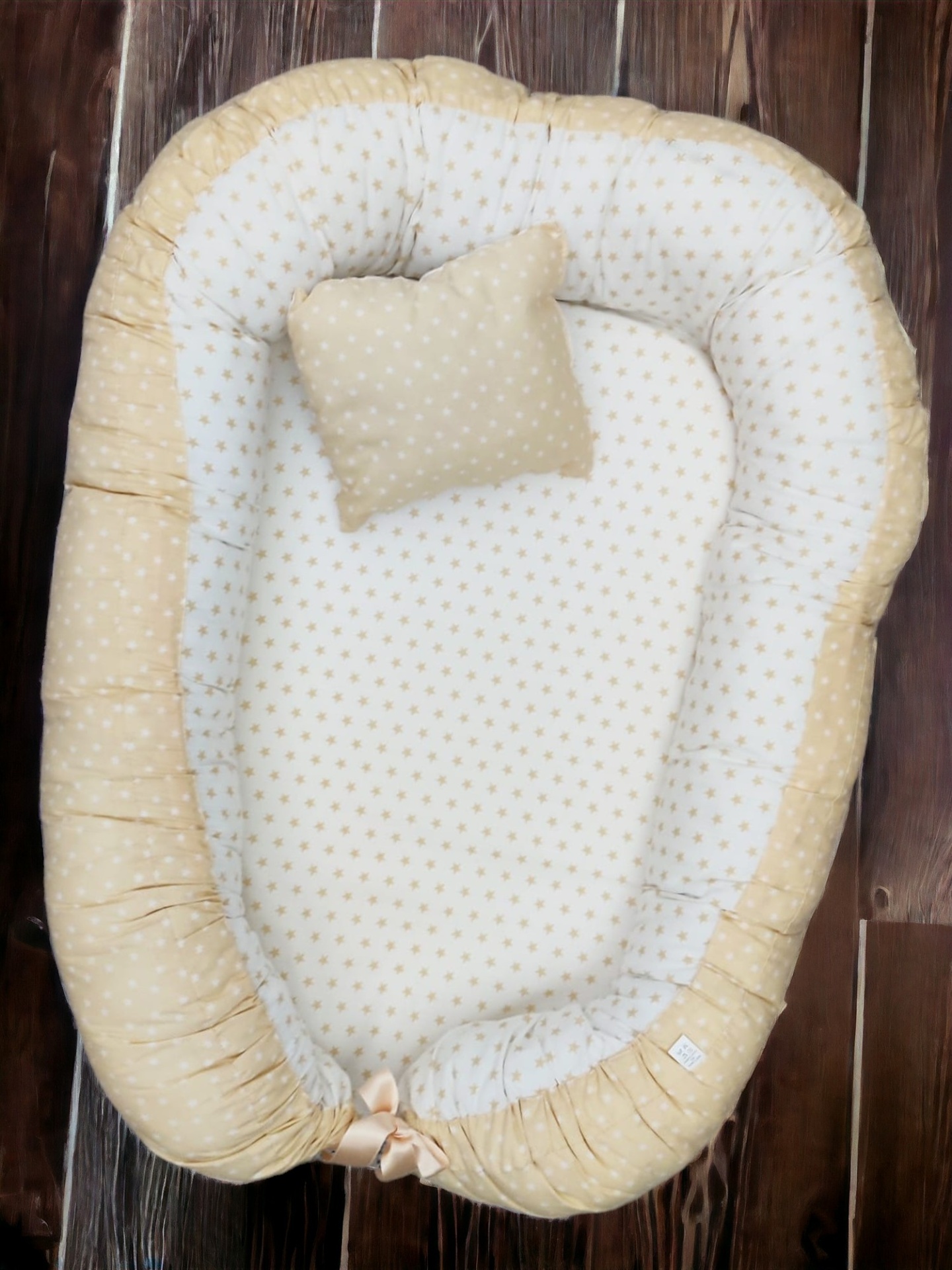 Ninho e almofada de bebé bege e branco com padrão de estrelas, sobre chão de madeira escura
