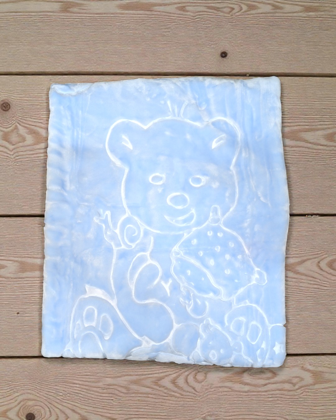 Manta azul clara com padrão de urso em relevo numa superfície de madeira.