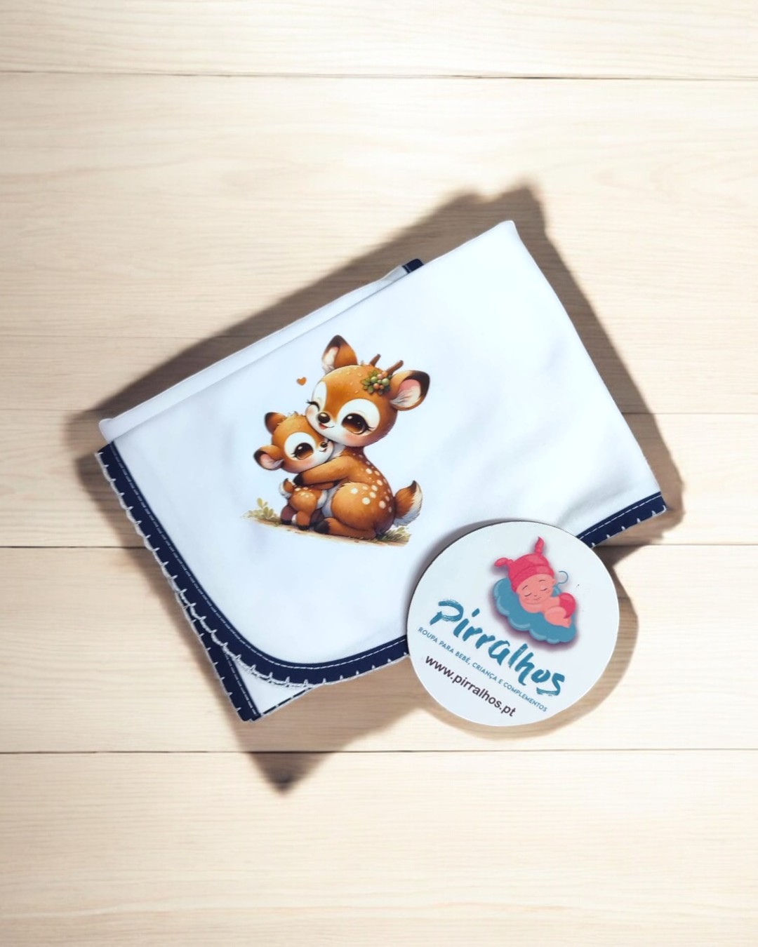 Fralda branca com borda azul escura e desenho de dois veados caricaturados, etiqueta redonda com o texto Pirralhos