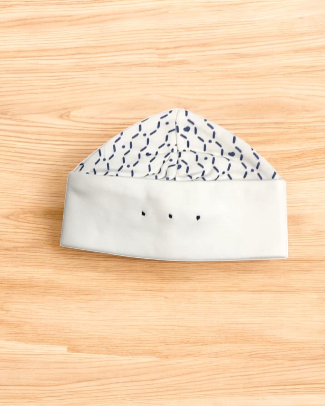 Gorro branco com padrão azul escuro sobre madeira clara