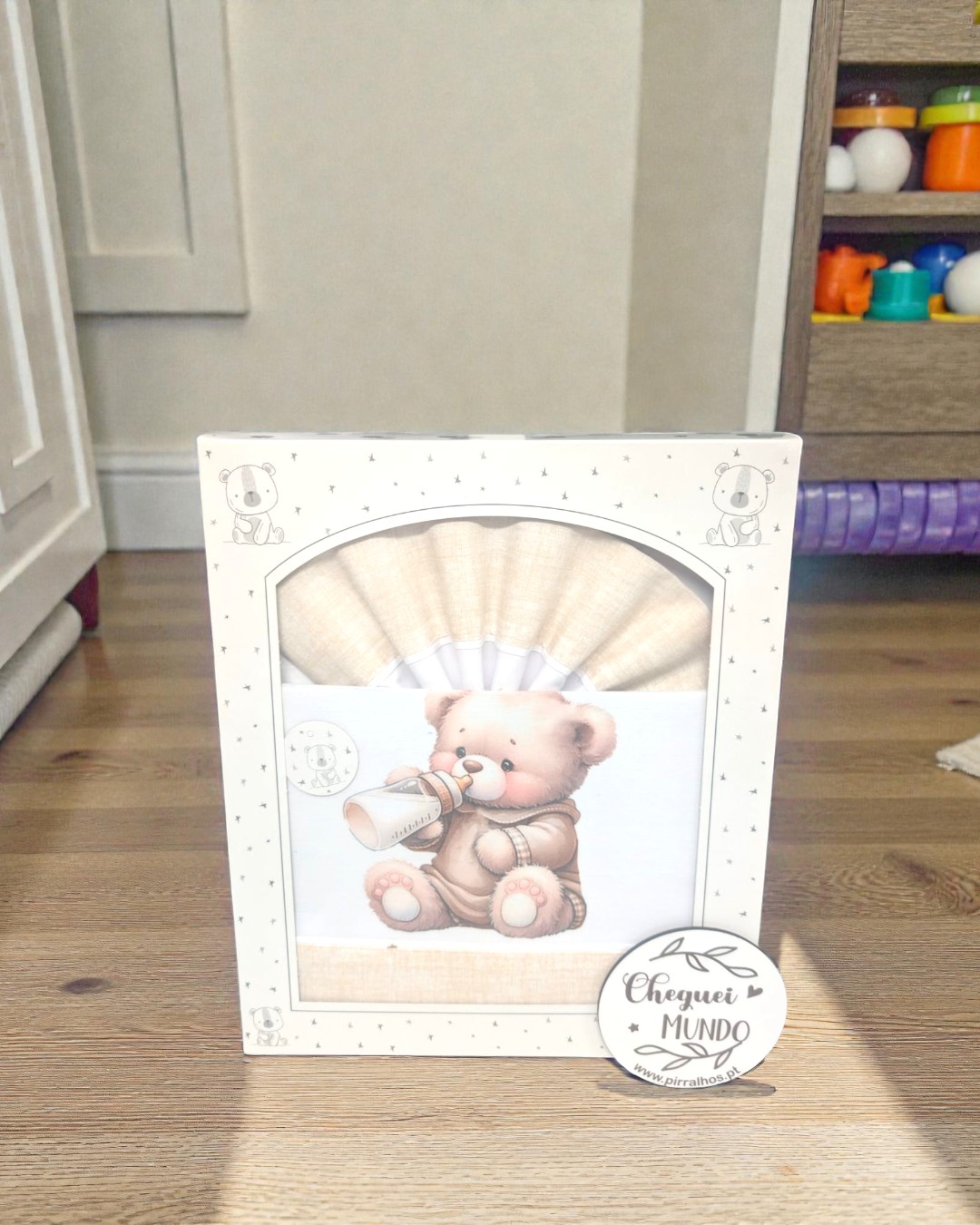 Caixa branca decorada com estrelas e ursinhos, contendo conjunto têxtil com desenho de ursinho a beber de mamadeira