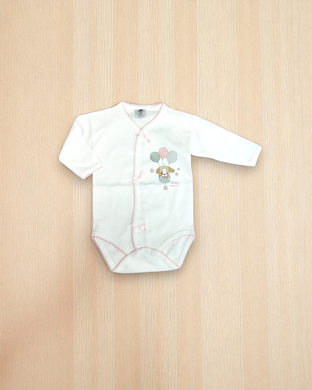 Body de bebé branco com ursinho e balões, sobre superfície de madeira clara