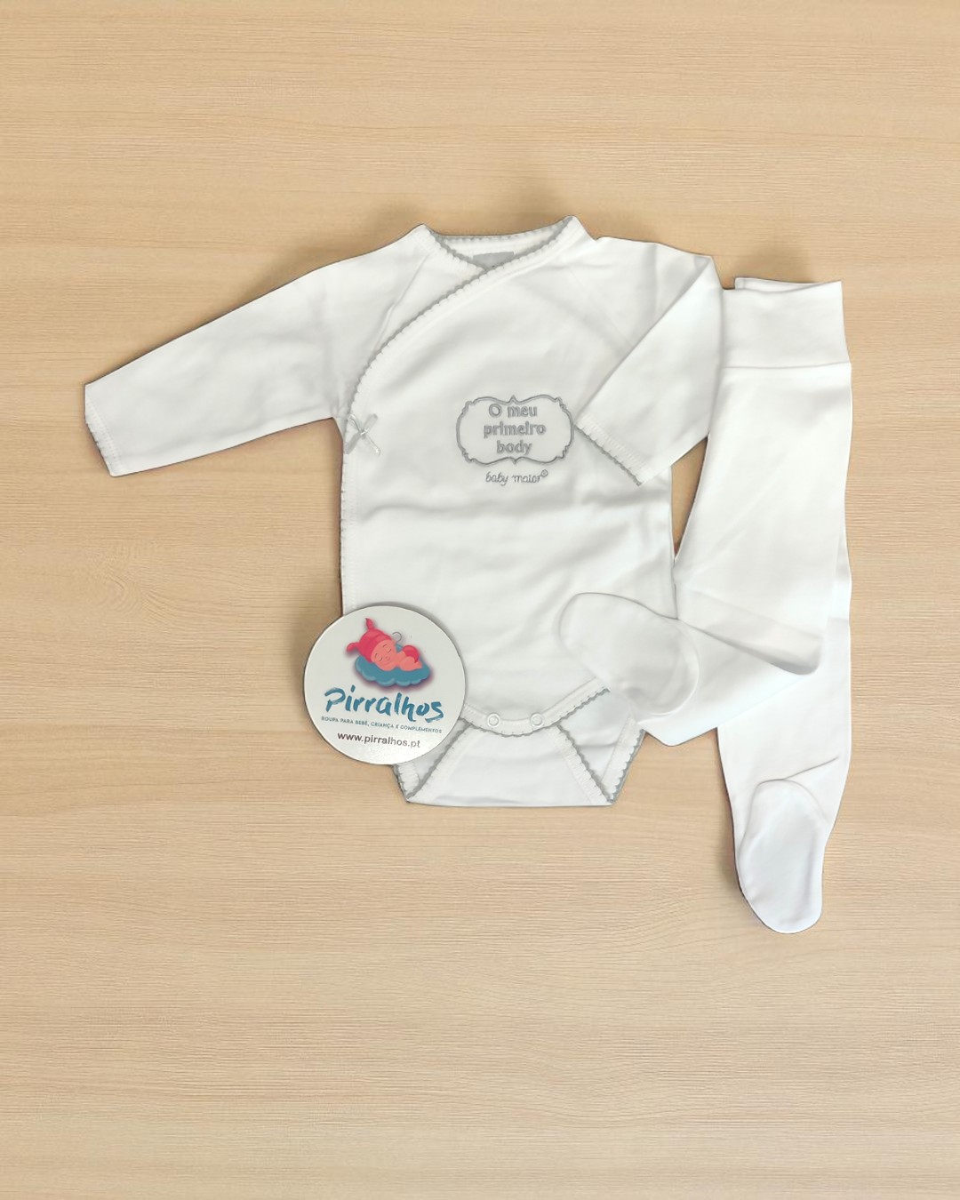 Conjunto de bebé branco com body e calças sobre superfície de madeira clara