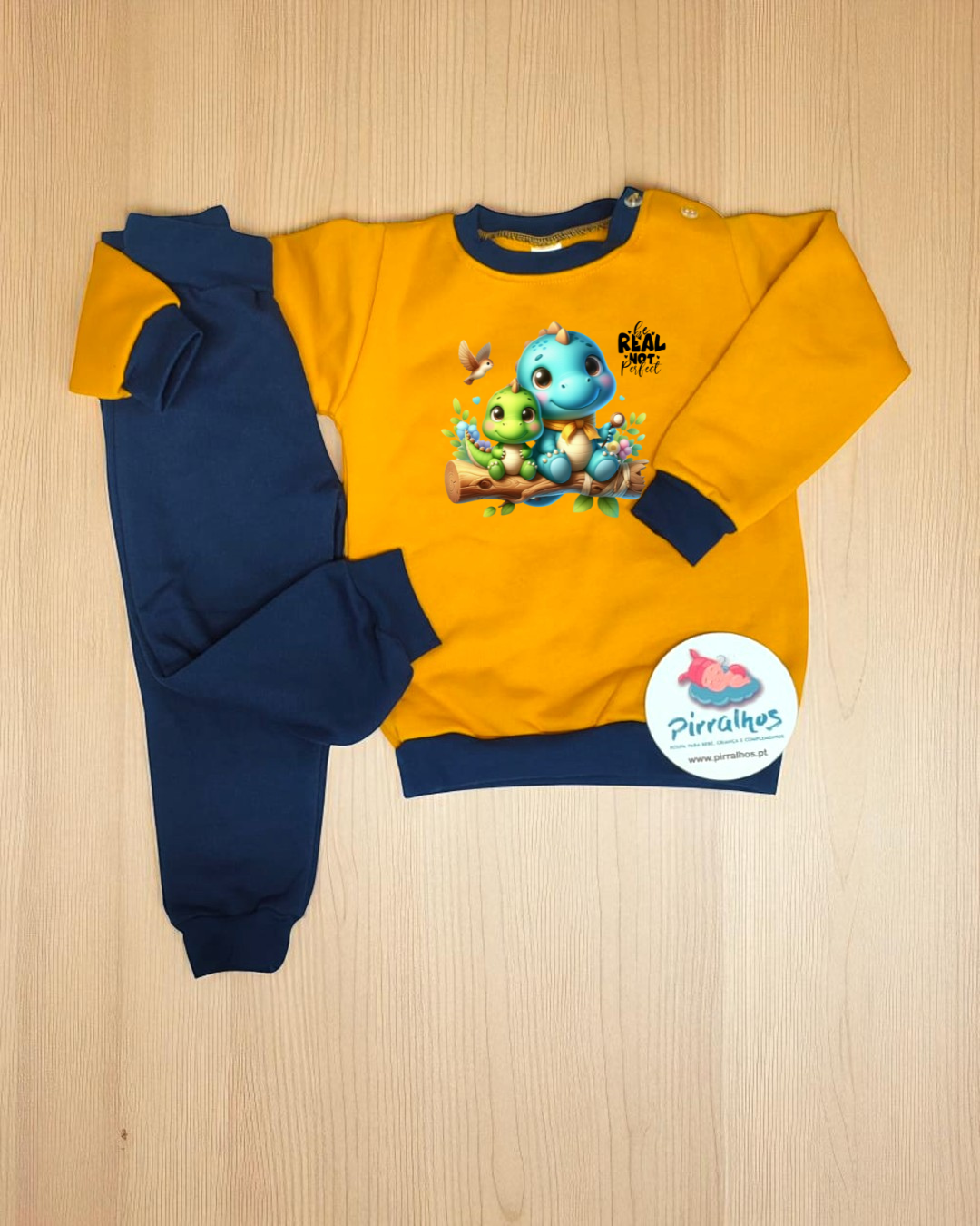 Conjunto de roupa infantil amarelo-mostarda e azul escuro com estampa de dinossauros e texto REAL TIME
