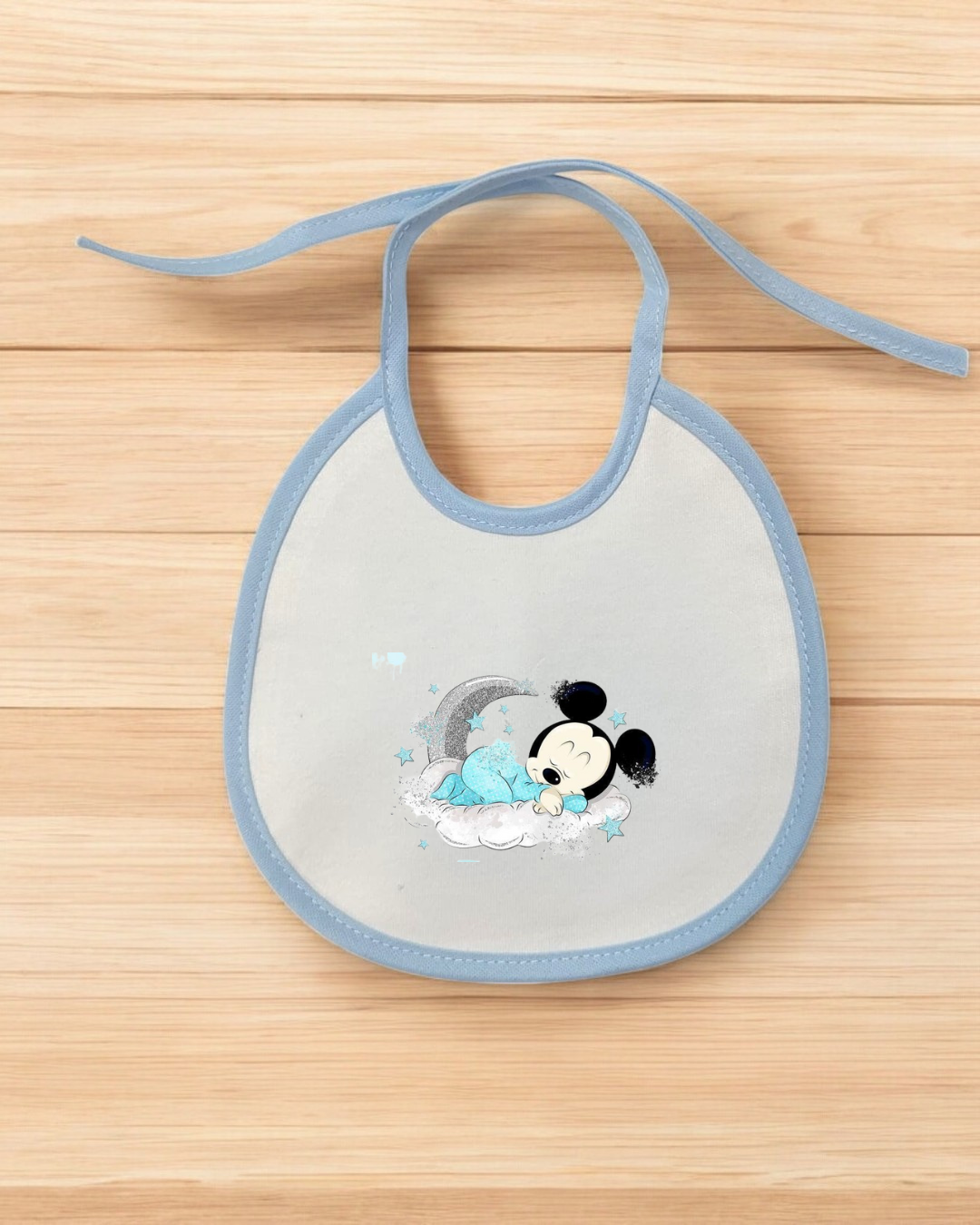 Babete branco com borda azul claro e ilustração de personagem semelhante a Mickey a dormir.