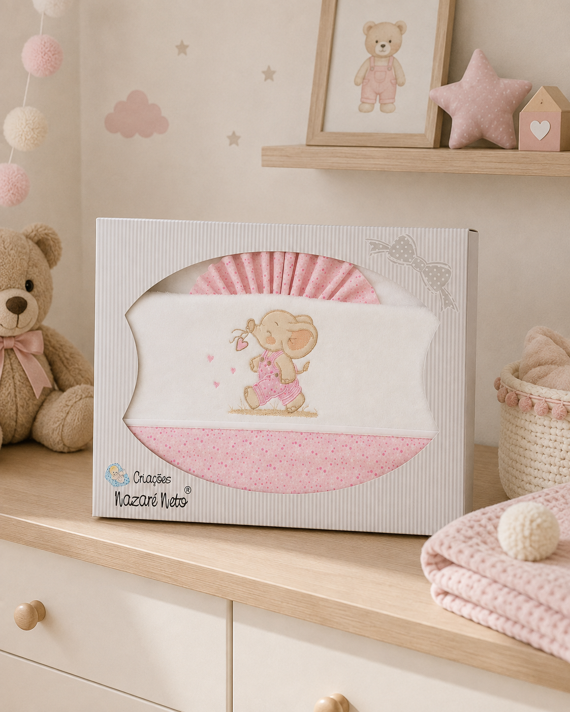 Conjunto de roupa de bebé rosa e branco com elefante, em caixa branca sobre móvel de madeira