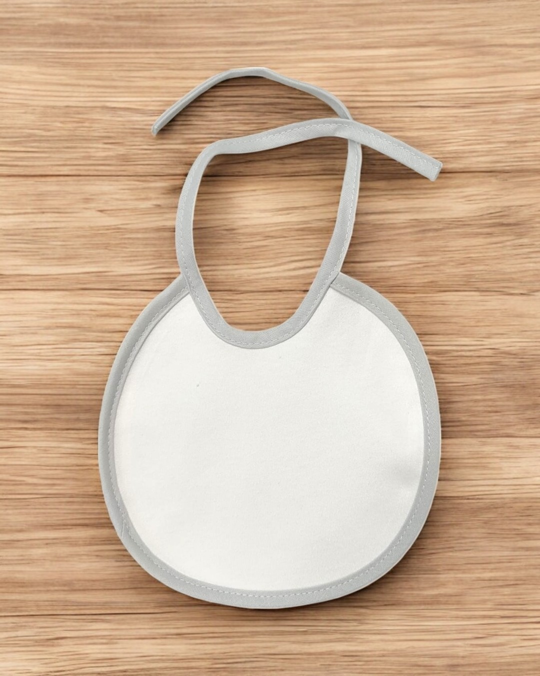 Babete de bebé branco com bordas cinzentas em superfície de madeira