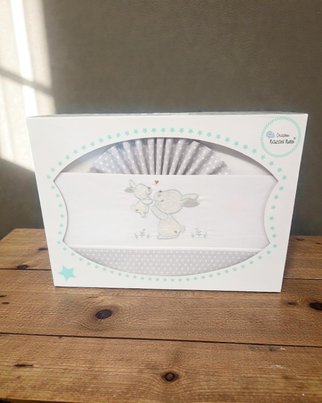 Conjunto de roupa de bebé com coelhos bordados e embalagem branca com estrelas azuis