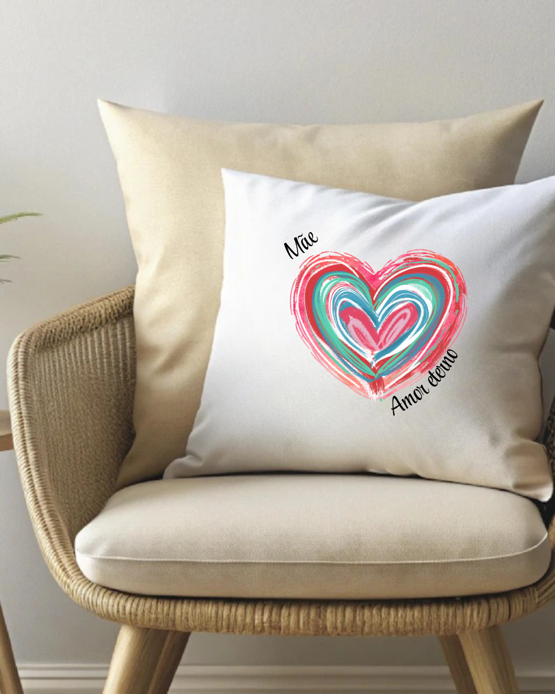 Almofada branca com estampa de coração colorido e texto, numa cadeira de rattan com almofada bege.