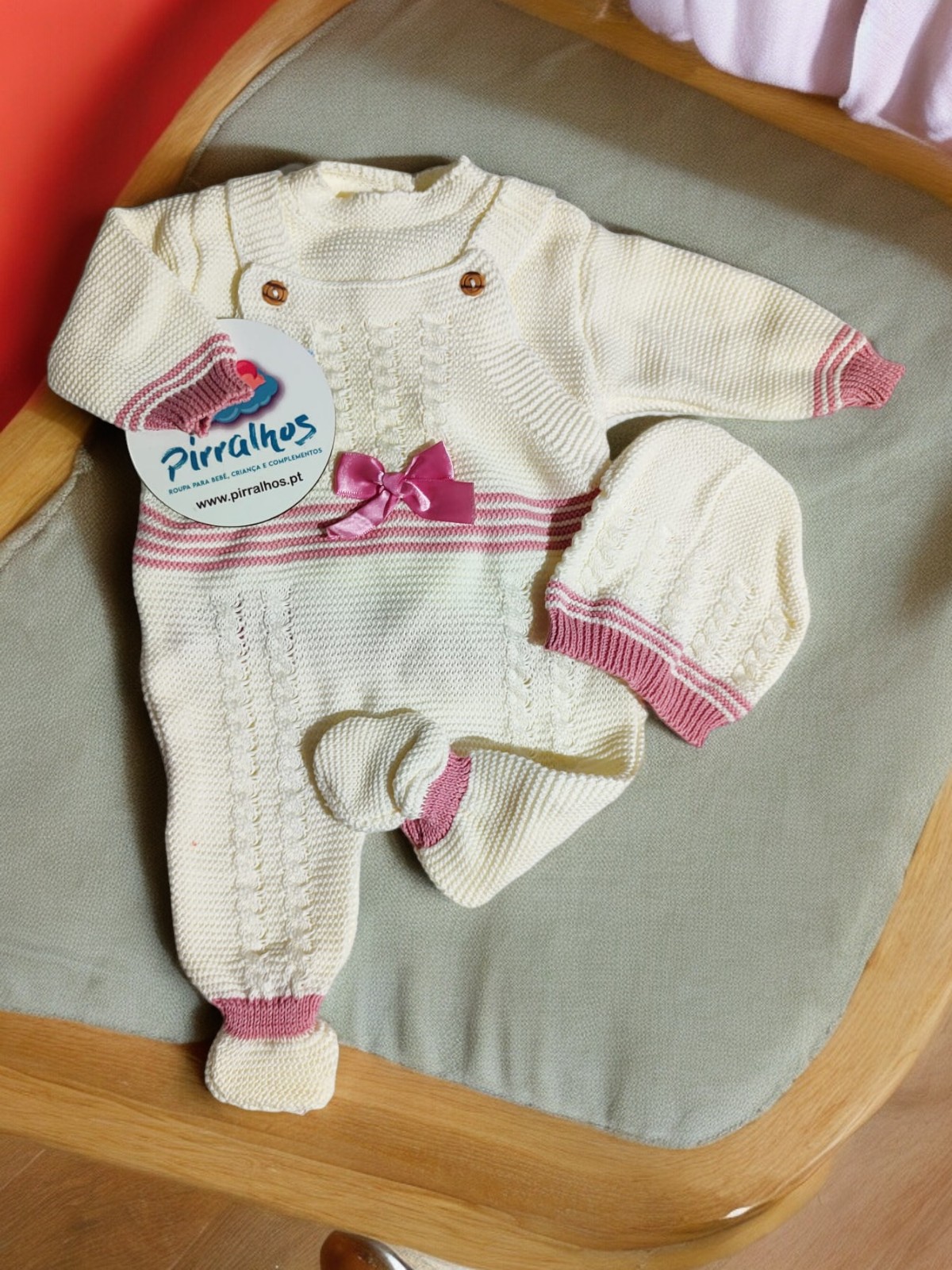 Conjunto de roupa para bebé em malha creme com detalhes em rosa e etiqueta da marca