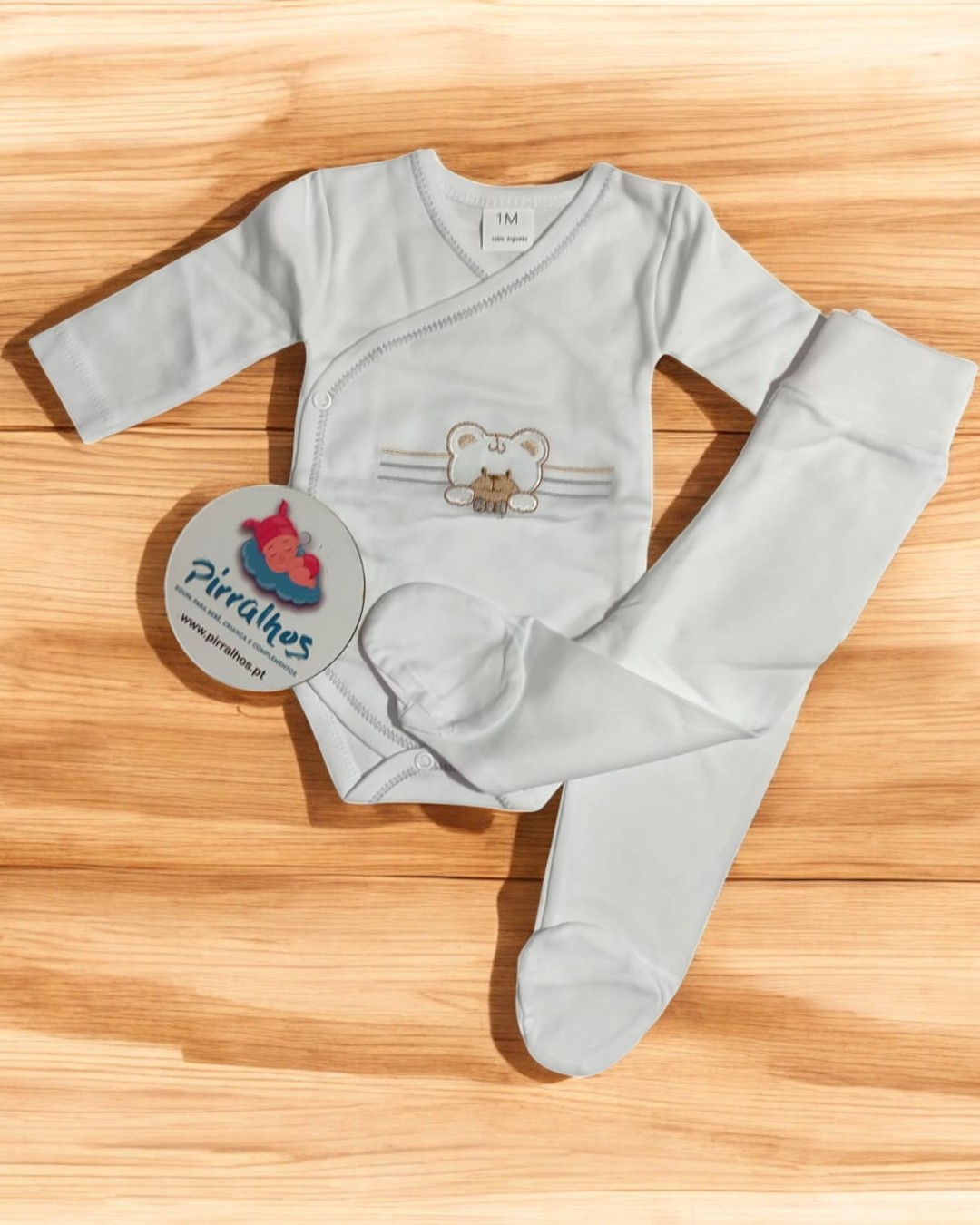 Conjunto branco de bebé com body e calças, sobre madeira clara