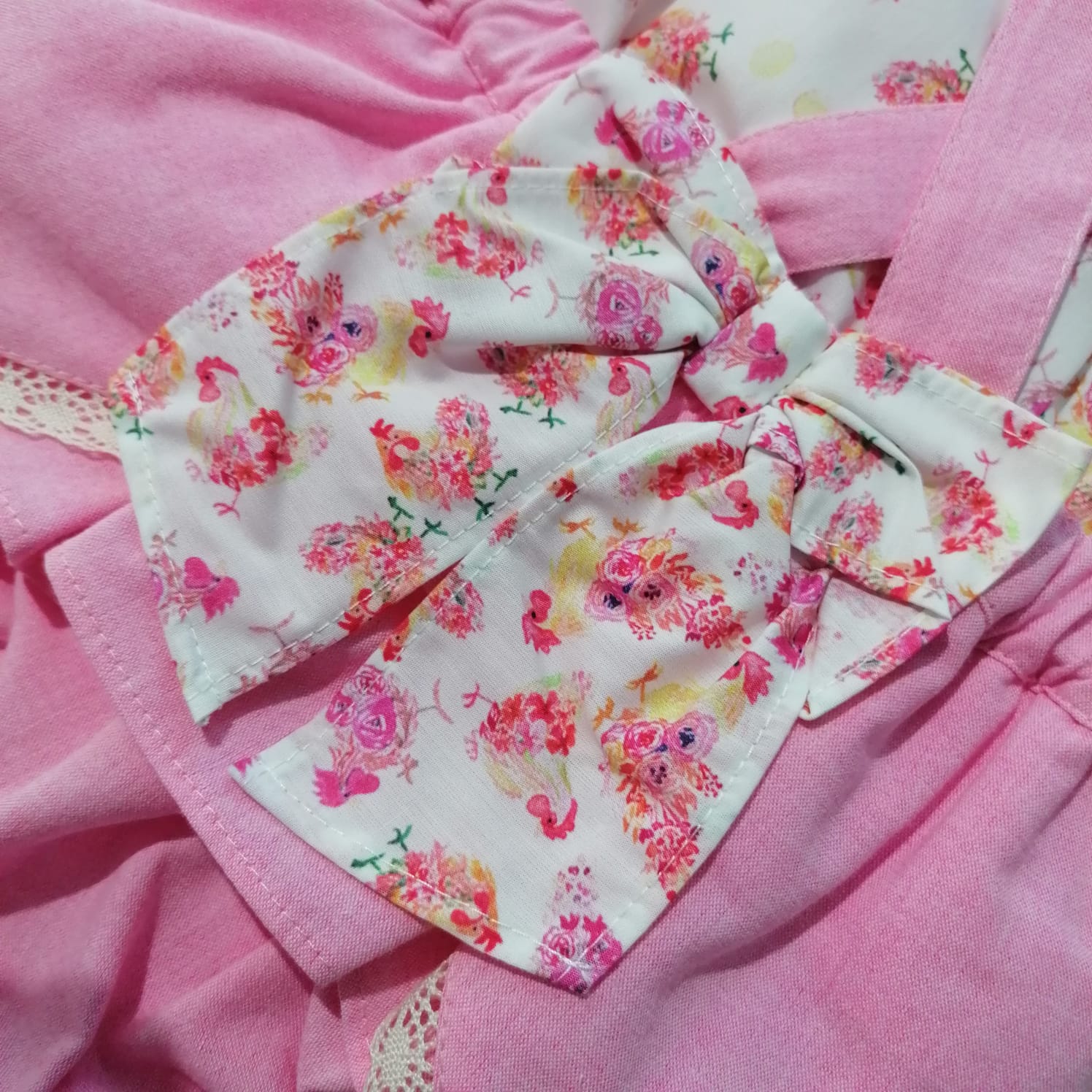 Roupa infantil rosa com laço branco estampado de flores coloridas