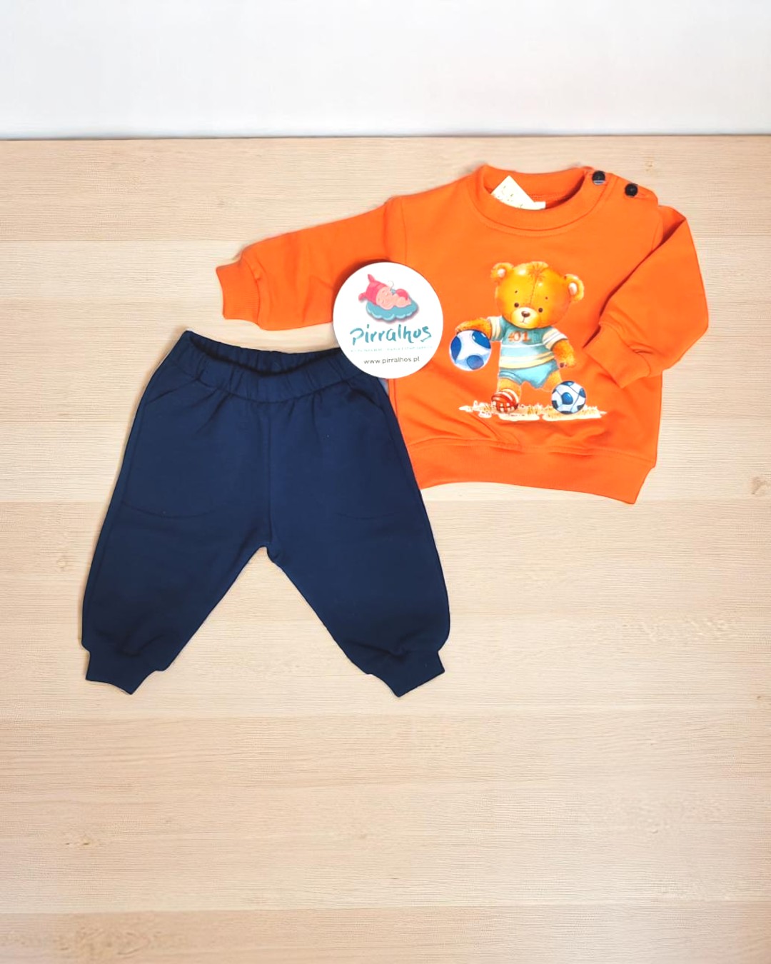 Conjunto de roupa infantil laranja e azul com estampa de urso e bolas de futebol