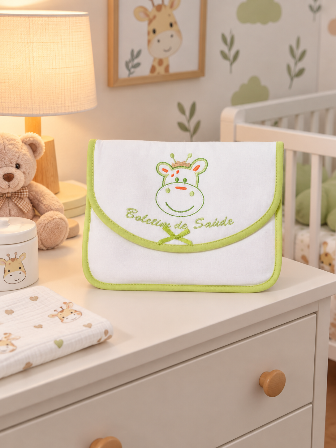 Bolsa branca e verde com bordado de girafa e texto Boletim de Saúde sobre cómoda com artigos para bebé