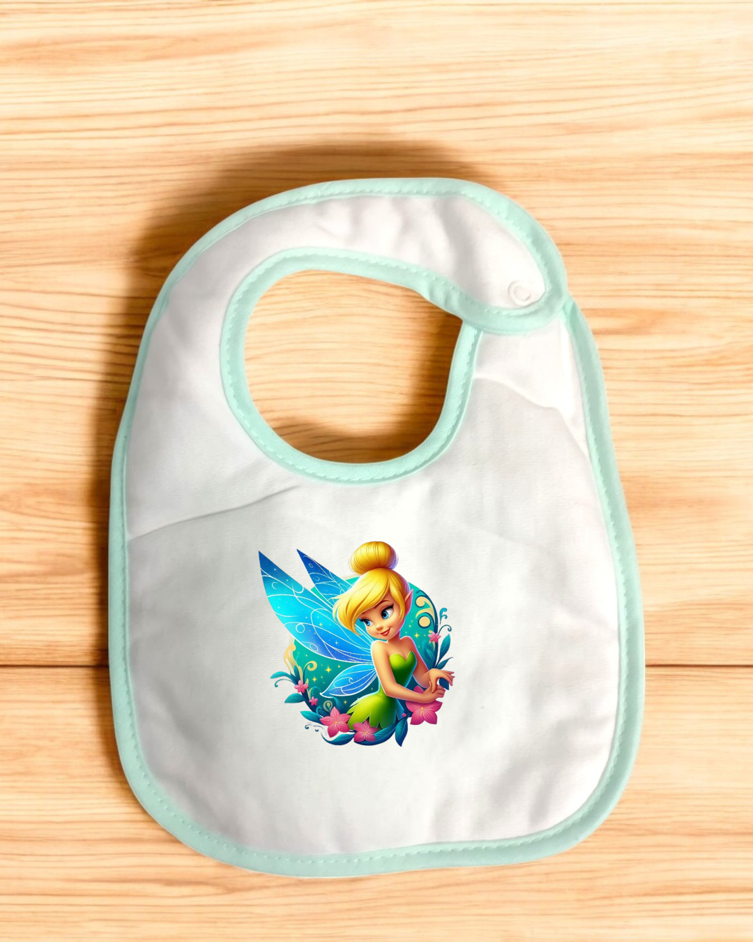 Babete branco com fada colorida e bordas verdes sobre fundo de madeira clara