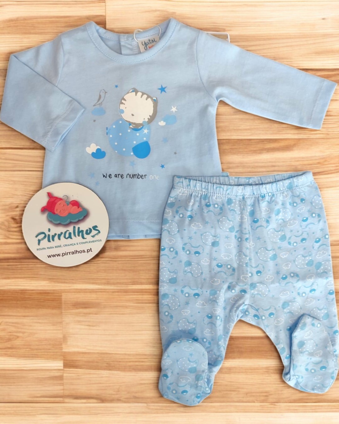 Conjunto de bebé azul claro com estampa de bebé e estrelas, calças estampadas com peixes, com etiqueta da marca Pirralhos