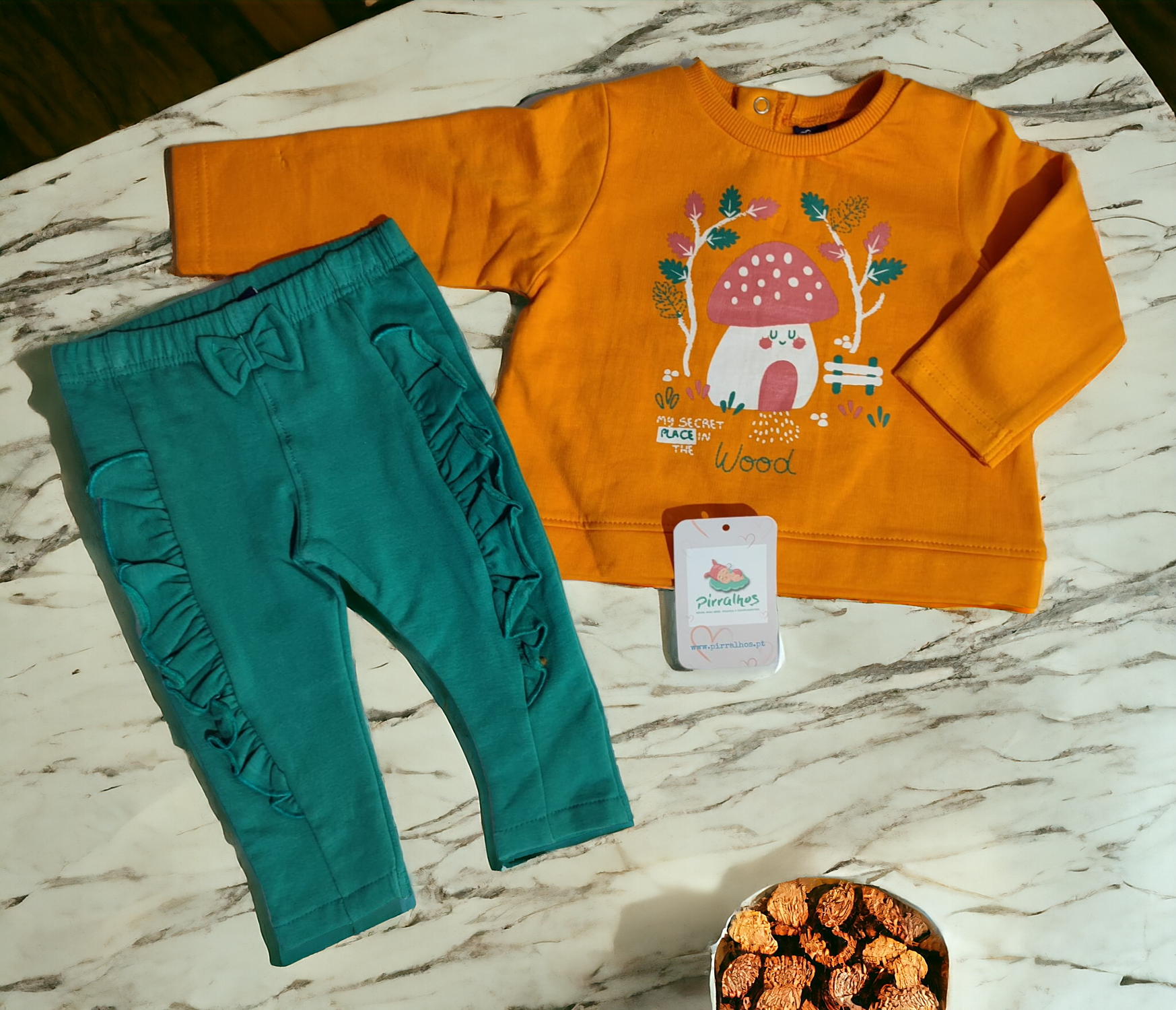 Conjunto infantil com camisola laranja estampada e calças verdes com folhos