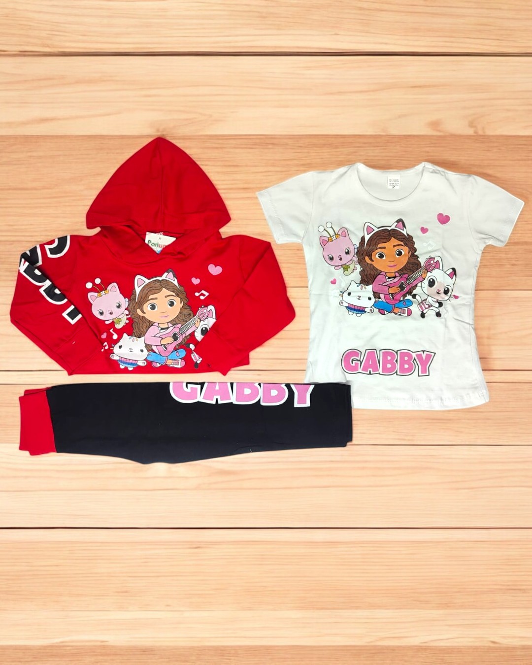 Conjunto infantil com camisola vermelha, t-shirt branca e calças pretas com estampa da personagem Gabby